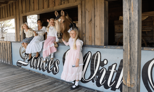 Girls dressed in 19th century costumes pose with a prop horse at the Dances with Wolves exhibit in 1880 Town